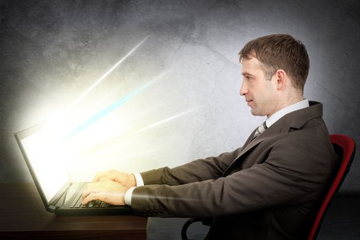 Cropped shot view of young businessman in front of table with laptop. E-business concept. Man in suit typing text on laptop. Monitor of laptop shine rays of light