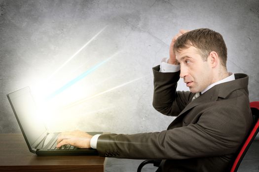 Serious man in suit sitting at table and typing on laptop with light coming through screen