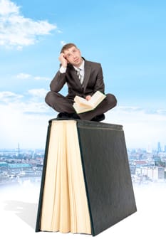 Man sitting on book and reading. Blue sky and city at background. Concept of reading