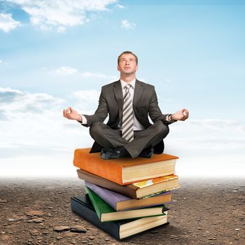 Young businessman sitting on pile of books and meditating. Education concept