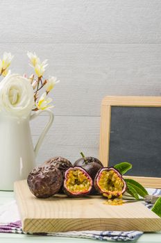 Passion fruits with leaves, knife and white flowers in jar on the vintage wooden table.