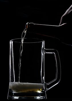 Serving beer in empty glass from bottle on black 