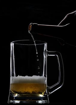 beer come from bottle in empty glass on black