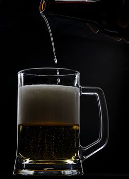 Last beer drops go in glass from bottle on black