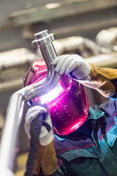 Industrial worker with protective mask welding inox elements in steel structures manufacture workshop.