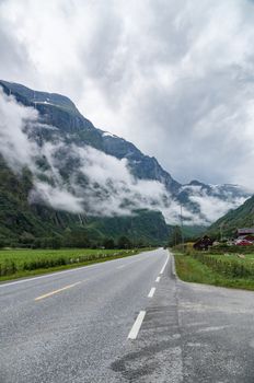 Misty mountains covered by clouds and vanishing road near Gudvangen village, Norway