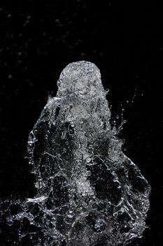 Fountain transparent water stream, splash and drops in motion over black background