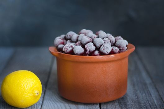 Frozen cherries in a ceramic dish, and lemon.Beavertail gray-blue background, rustic style.