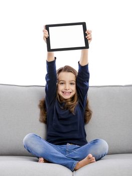 Happy little girl sitting on a couch and using a tablet