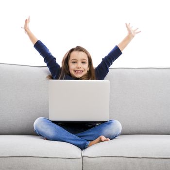 Happy little girl sitting on a couch and working a laptop