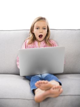 Happy little girl sitting on a couch and working a laptop