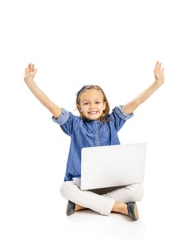 Happy little girl sitting on the floor and working a laptop