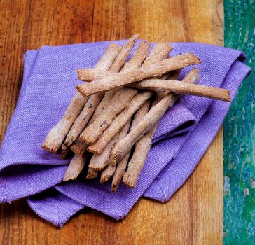 Freshly Baked Whole Wheat Bread Sticks on Purple Napkin closeup on Wooden Cutting Board