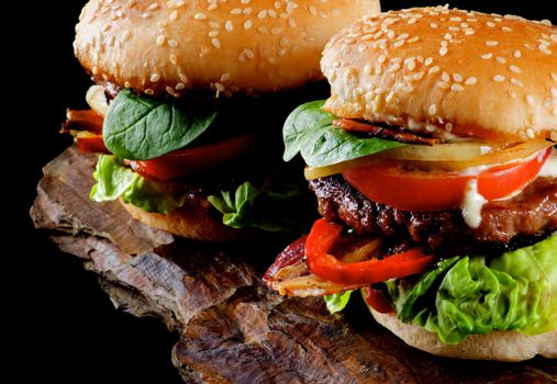 Two Tasty Hamburgers with Beef, Bacon, Lettuce, Tomatoes, Basil, Roasted Onion and Juicy Sauce on Sesame Buns Cross Section on Stone Board 