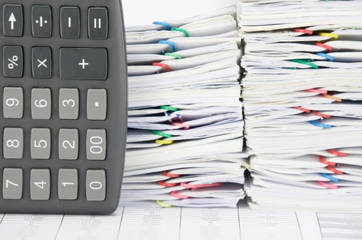 Black calculator place vertical on finance account have overload of paperwork with colorful paperclip as background.