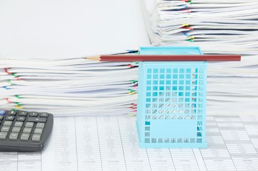 House in blue basket with brown pencil on top and calculator on finance account have overload of paperwork with colorful paperclip as background.