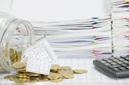 House with stack of gold coins flowing out of bottle on finance account have calculator and overload of paperwork as background.