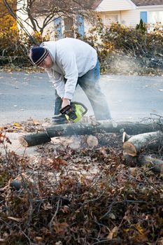 Man cutting tree limbs with a chainsaw that have fallen from storm damage.  A late fall snow storm in the month of October was the cause.