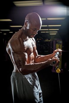 Body builder working out at the gym doing exercises on the cable machine under dramatic lighting.
