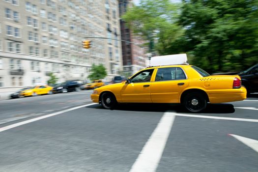 Yellow NYC taxi cab speeding by during daytime.  Slow shutter speed panning technique used for motion blur.