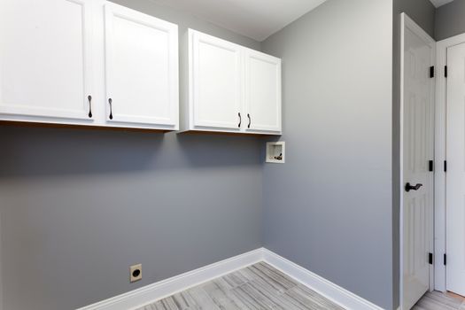 Empty laundry room setup with electrical plumbling hookups and cabinets in a modern home. 