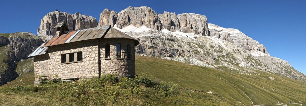 Church on the green grass at the foot of the massif of the Sella mountain range and blue sky in the background