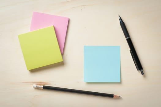 Sticky paper including blue, green, and pink color with blank area for text or message stick on wood table with pen and pencil