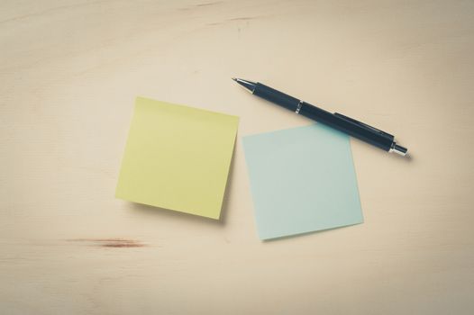 Sticky paper including blue, and green color with blank area for text or message stick on wood table with pen in morning time with vintage filter effect