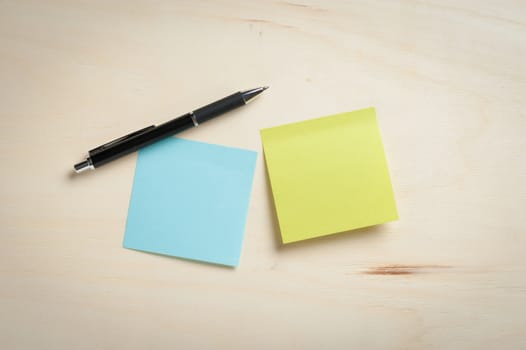 Sticky paper including blue, and green color with blank area for text or message stick on wood table with pen in morning time