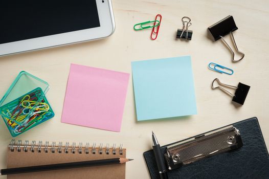 Sticky paper including blue, and green color with blank area for text or message stick on wood table with office supplies and small tablet pc