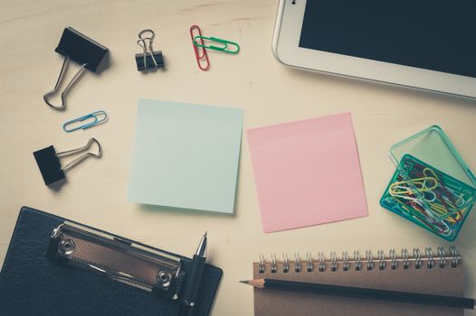 Sticky paper including blue, and green color with blank area for text or message stick on wood table with office supplies and small tablet pc in morning time with vintage filter effect