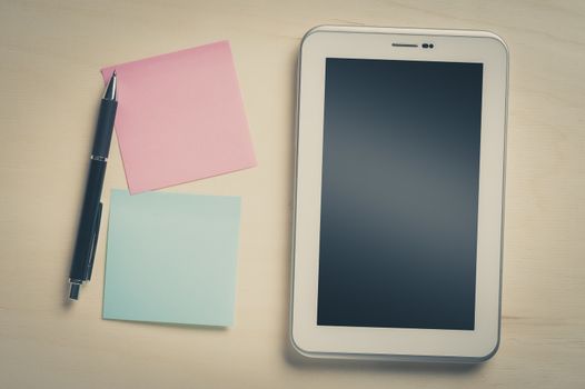 Small tablet pc with blank area on touchscreen and sticky paper with blank copy space on wood table with vintage filter effect