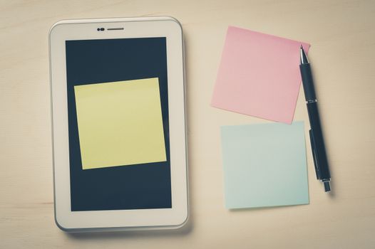 Yellow sticky paper with blank copy space stick on small tablet pc on wood table with vintage filter effect