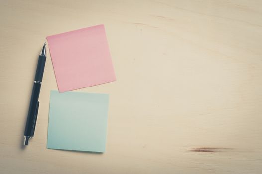 Sticky paper including blue, and pink color with blank area for text or message stick on wood table with pen, processed with vintage filter effect