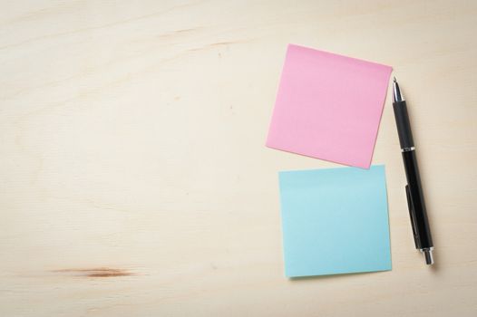 Sticky paper including blue, and pink color with blank area for text or message stick on wood table with pen