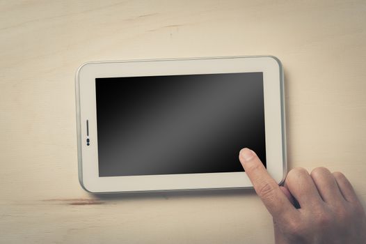 Young man right hand touching on small tablet with blank area on touchcreen on wood table