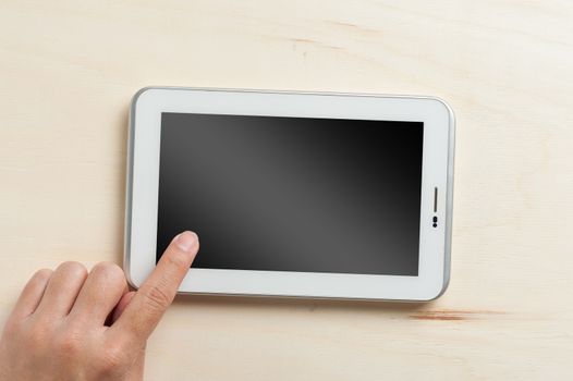 Young man left hand touching on small tablet with blank area on touchcreen on wood table