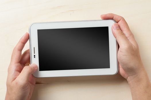 Young man hands holding small tablet with blank area on touchscreen on wood table
