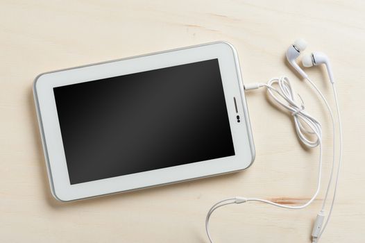 Small tablet pc with blank area on touchscreen and in ear headset on wood table