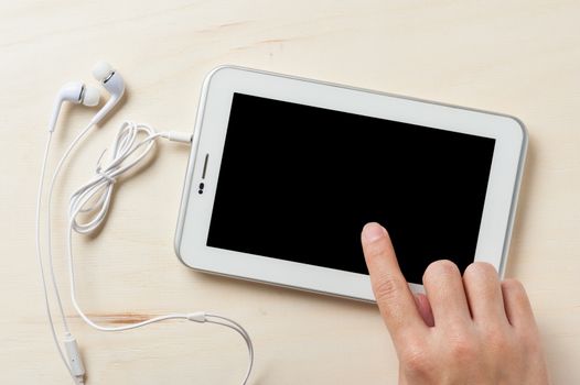 Young man hand touching on small tablet pc screen on wood table with in ear headset beside