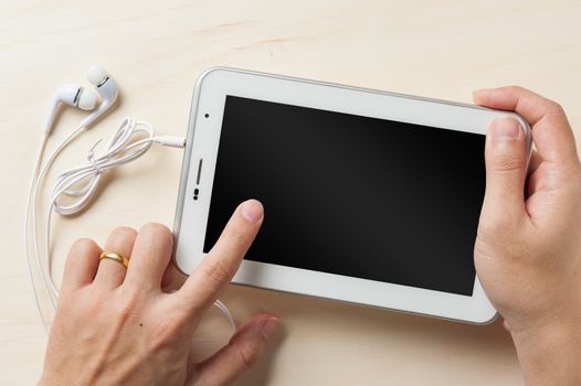 Young man hand touching on small tablet pc screen on wood table with in ear headset beside