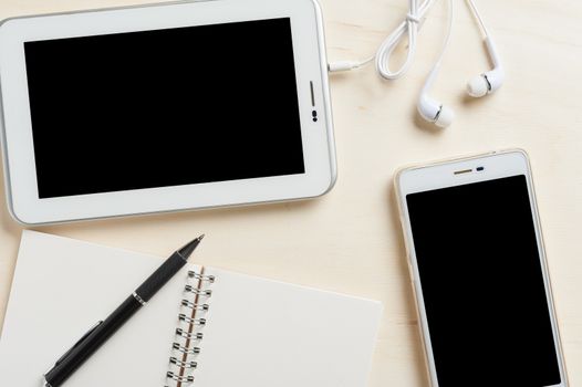 Small tablet pc with blank area on touchscreen, smart phone, in ear headset, notebook, and pen on wood table