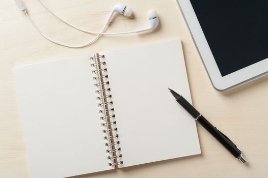 Notebook with blank area for text or message and pen beside small tablet pc and in ear headset on wood table