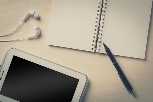 Notebook with blank area for text or message and pen beside small tablet pc and in ear headset on wood table