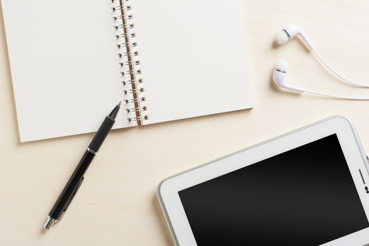 Notebook with blank area for text or message and pen beside small tablet pc and in ear headset on wood table