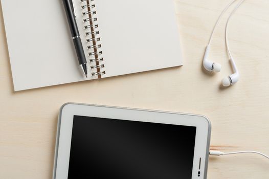 Notebook, pen, small tablet pc, and in ear headset on wood table