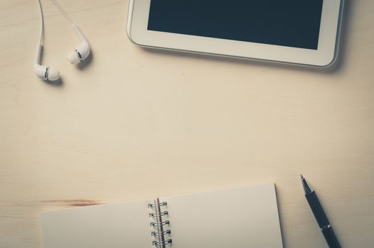 Notebook, pen, small tablet pc, and in ear headset on wood table with vintage filter effect