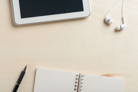 Notebook, pen, small tablet pc, and in ear headset on wood table