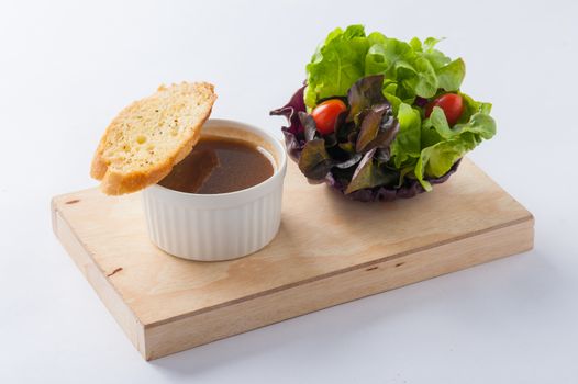 Onion soup in ceramic cup with toast and freash vegetables on wood plate. Clean and healthy eating concept food.