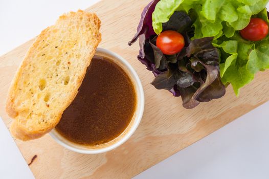 Onion soup in ceramic cup with toast and freash vegetables on wood plate. Clean and healthy eating concept food.